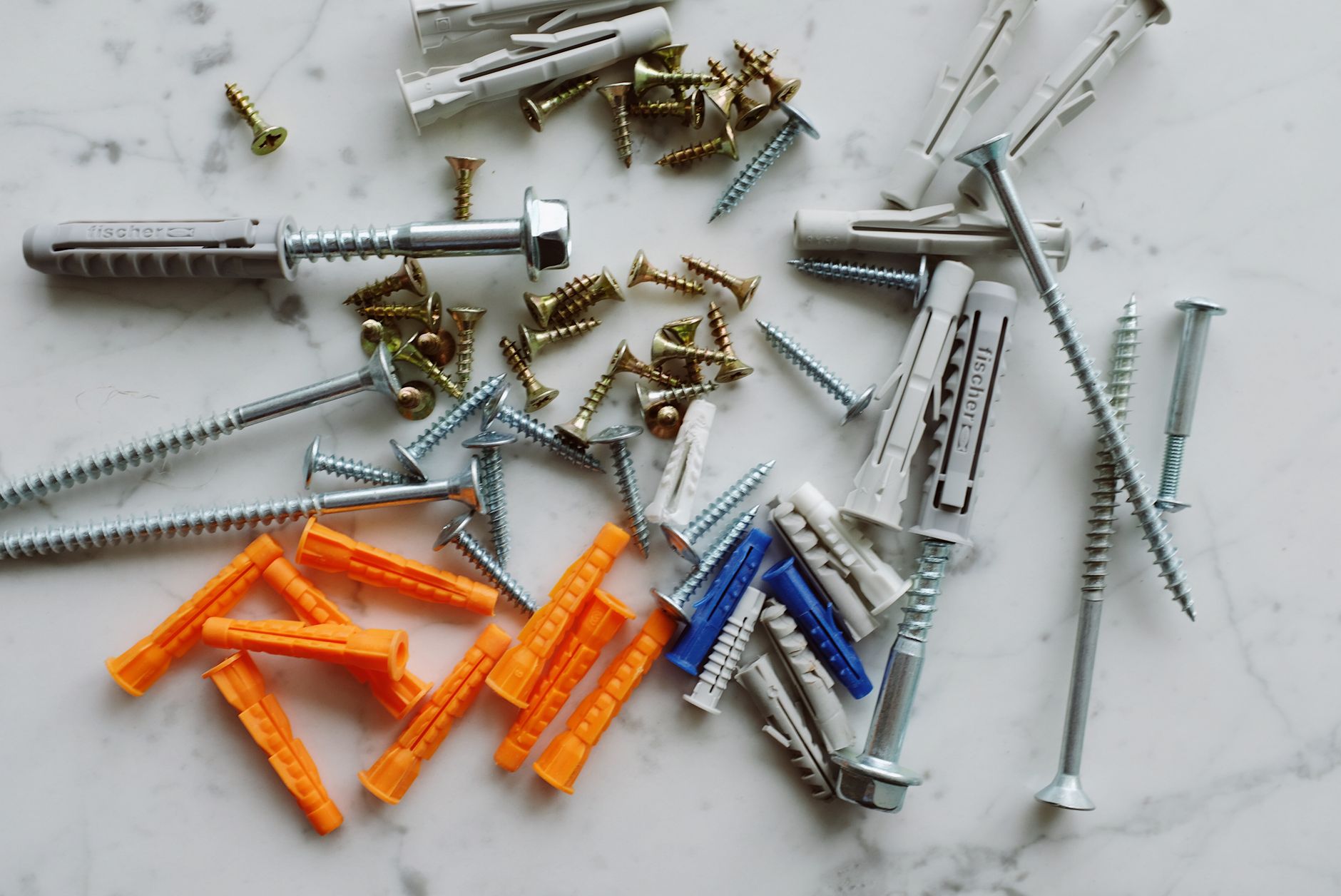Set of various multicolored plastic dowels with metal screws of different sizes placed on white marble table in modern worksh