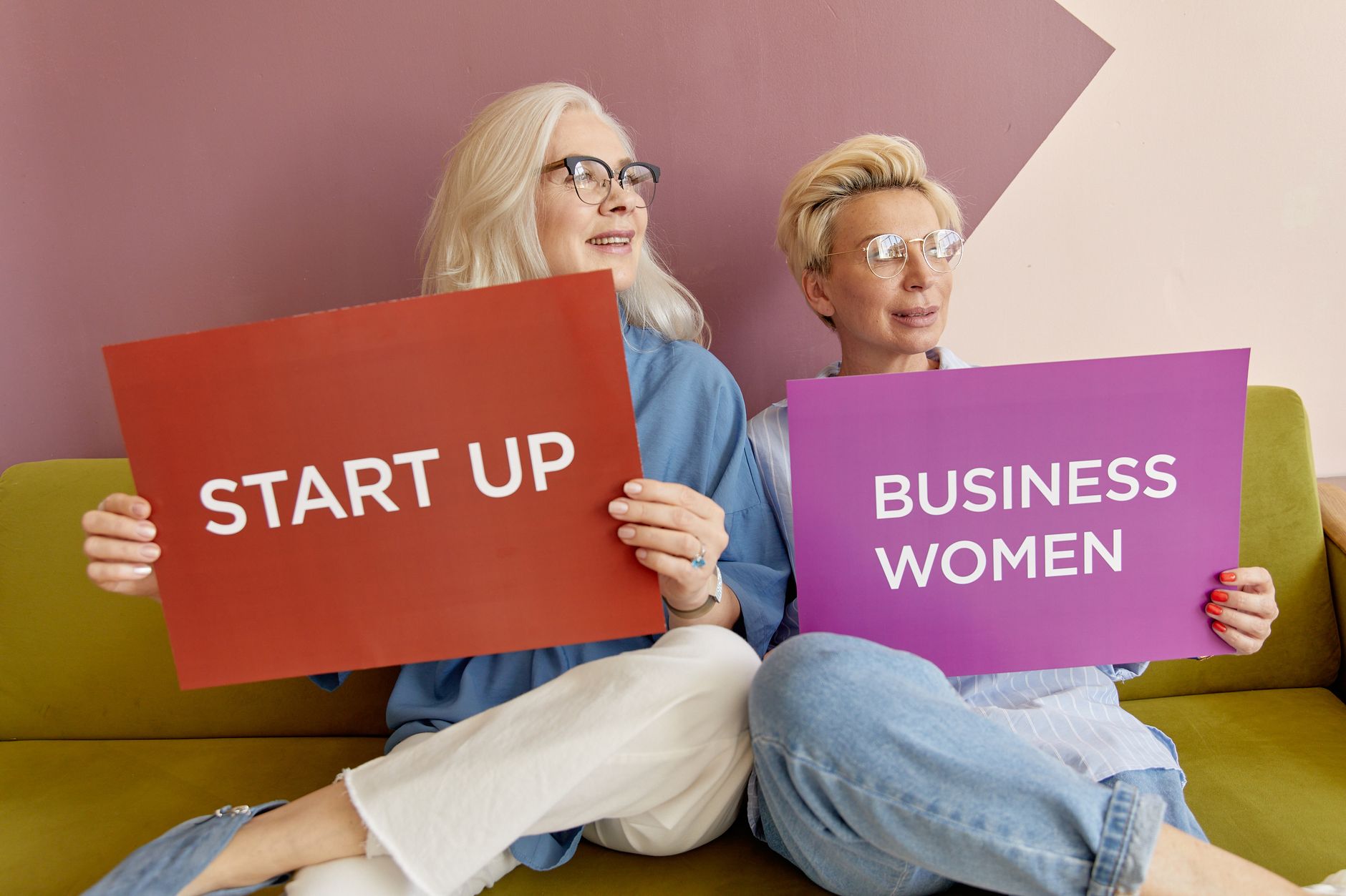 Two women on a sofa holding signs promoting startup and business women. — Make Leasing Easier with the Best Student Housing S