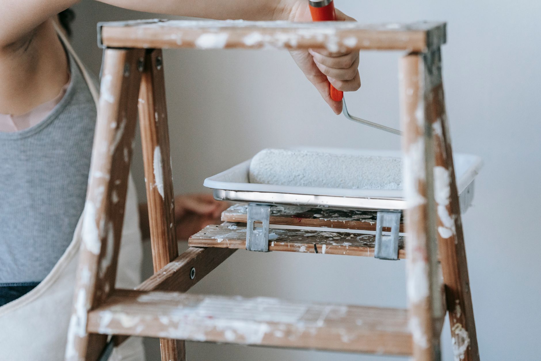 Adult woman using a roller and ladder to paint a room wall indoors. — Reliable Fire Protection Services In Charlotte, NC For