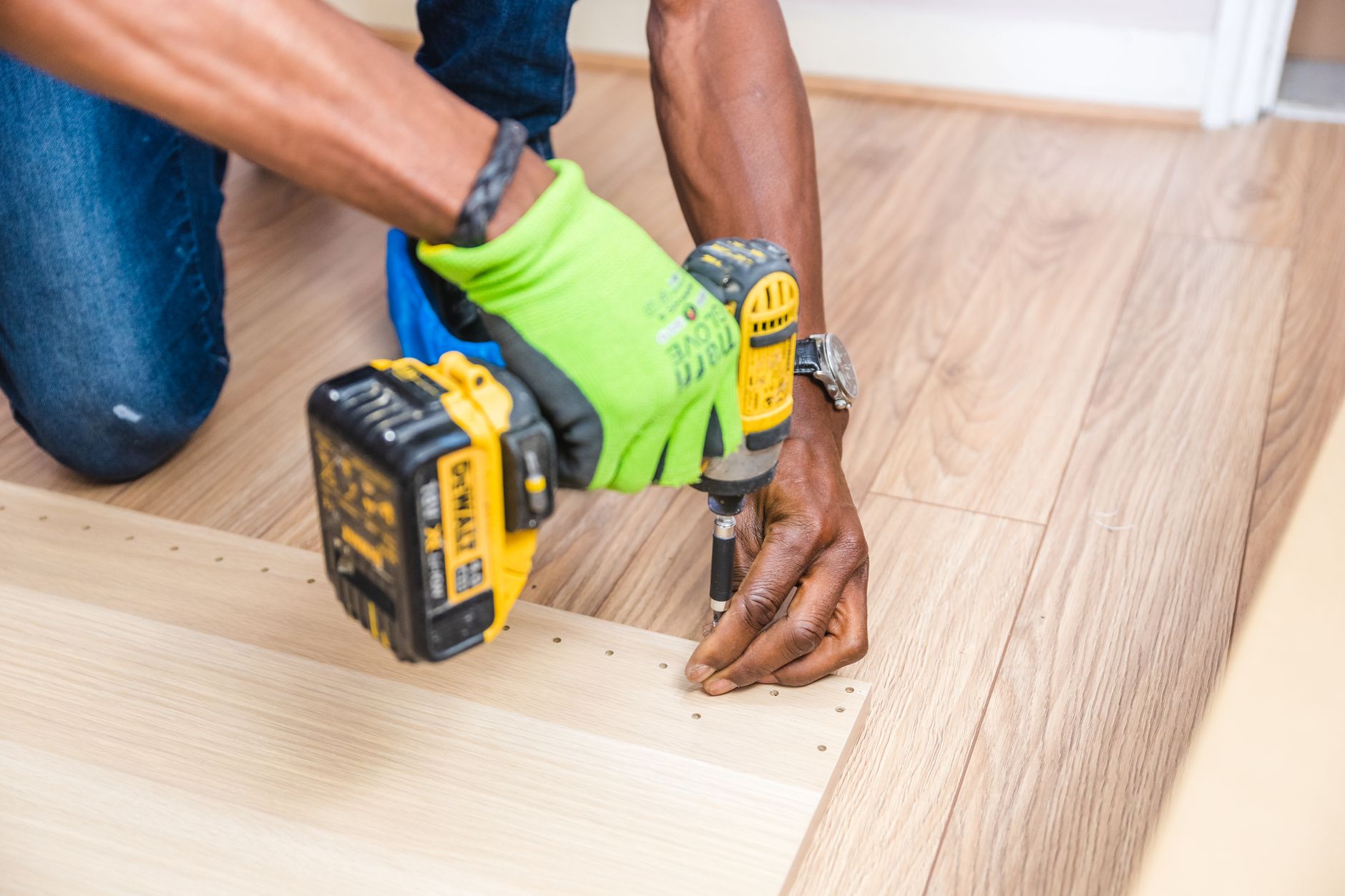Close-up of handyman drilling wood indoors with green gloves and cordless drill. — Reliable Plumbing Solutions You Can Trust