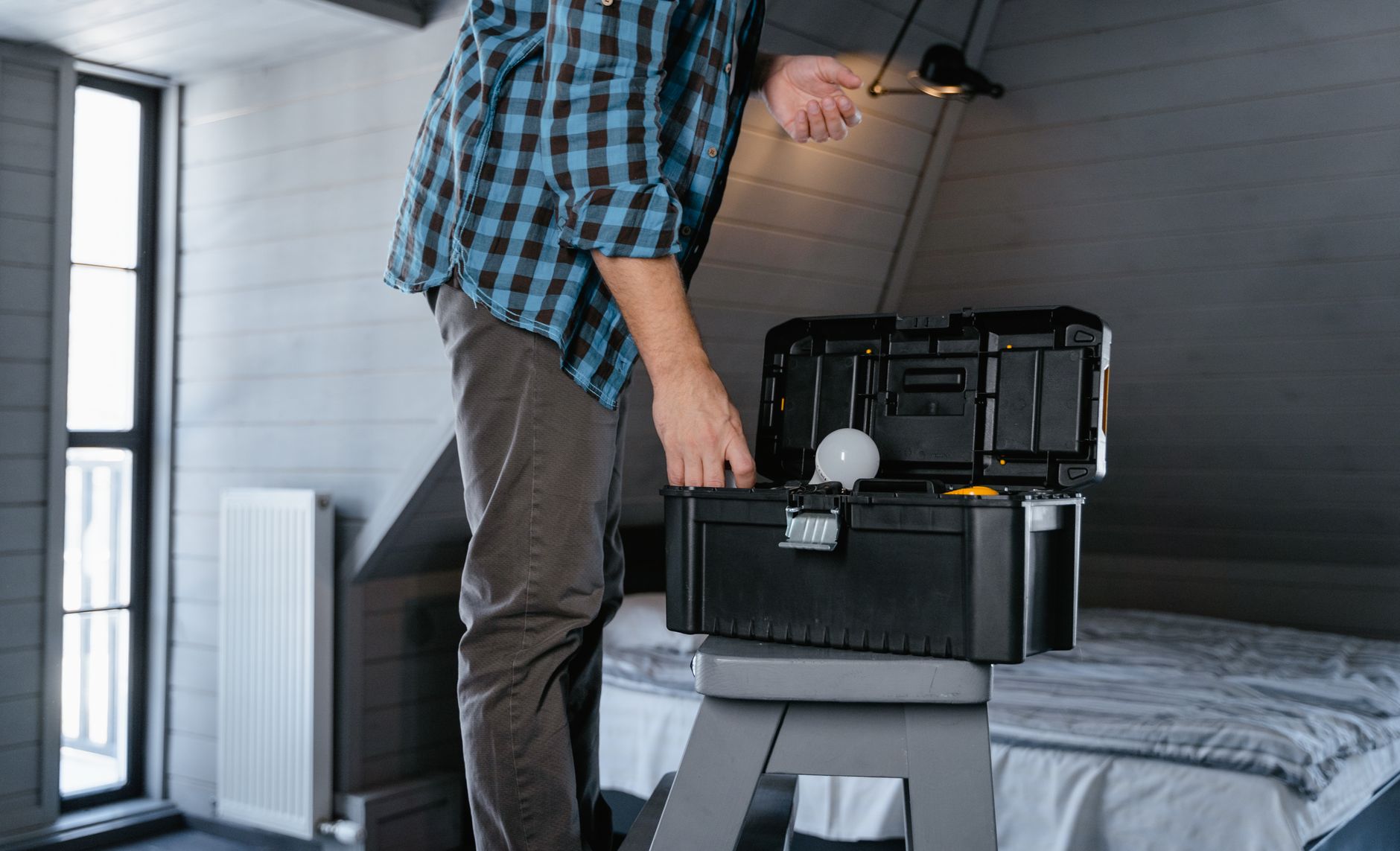 Person in plaid shirt fixing a light bulb using a toolbox in a rustic attic interior. — Transforming Landscapes with Retainin