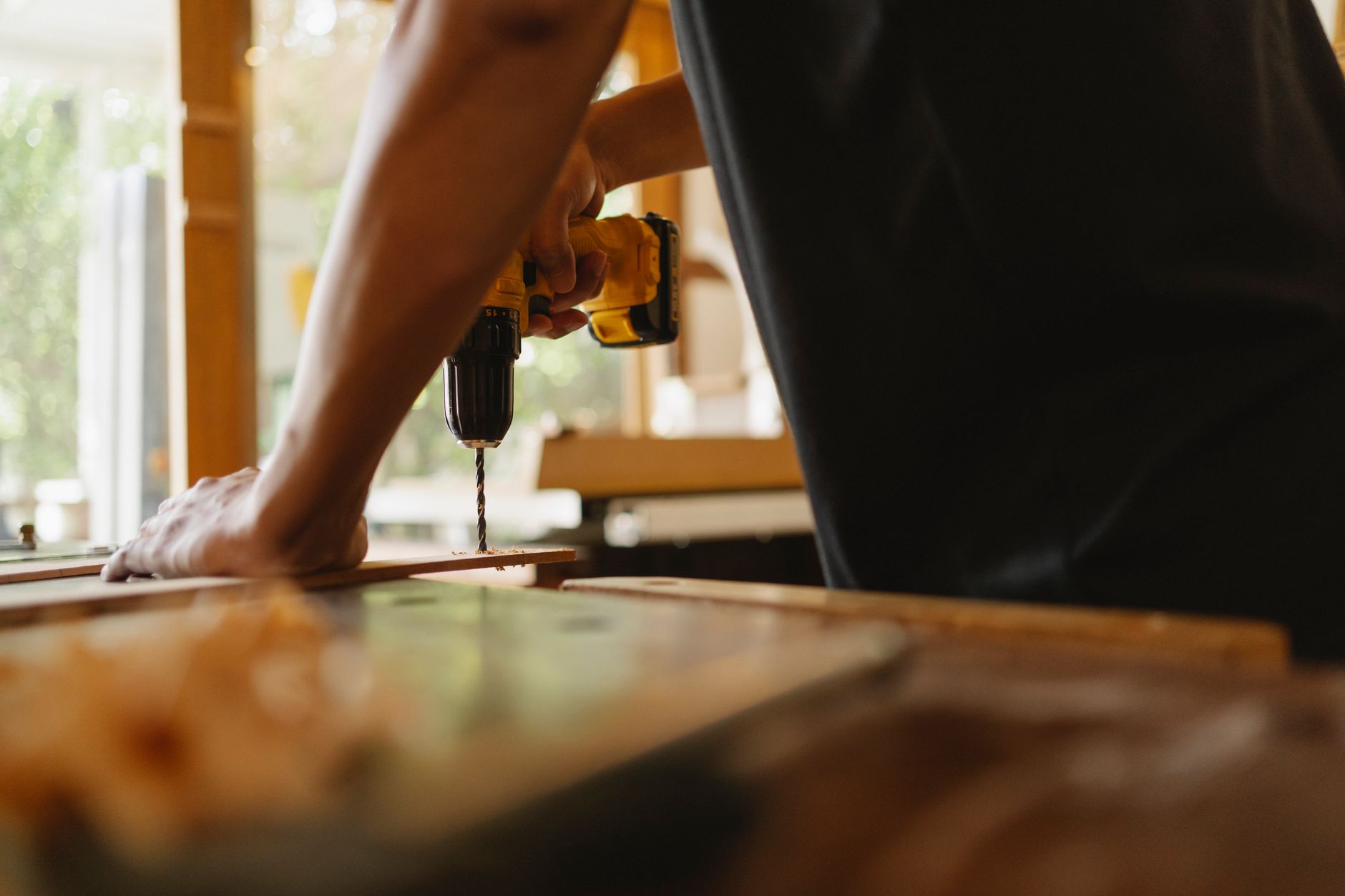 Crop anonymous male carpenter making hole on wooden plank with drill during work in studio on sunny day — Trusted Drywall Con