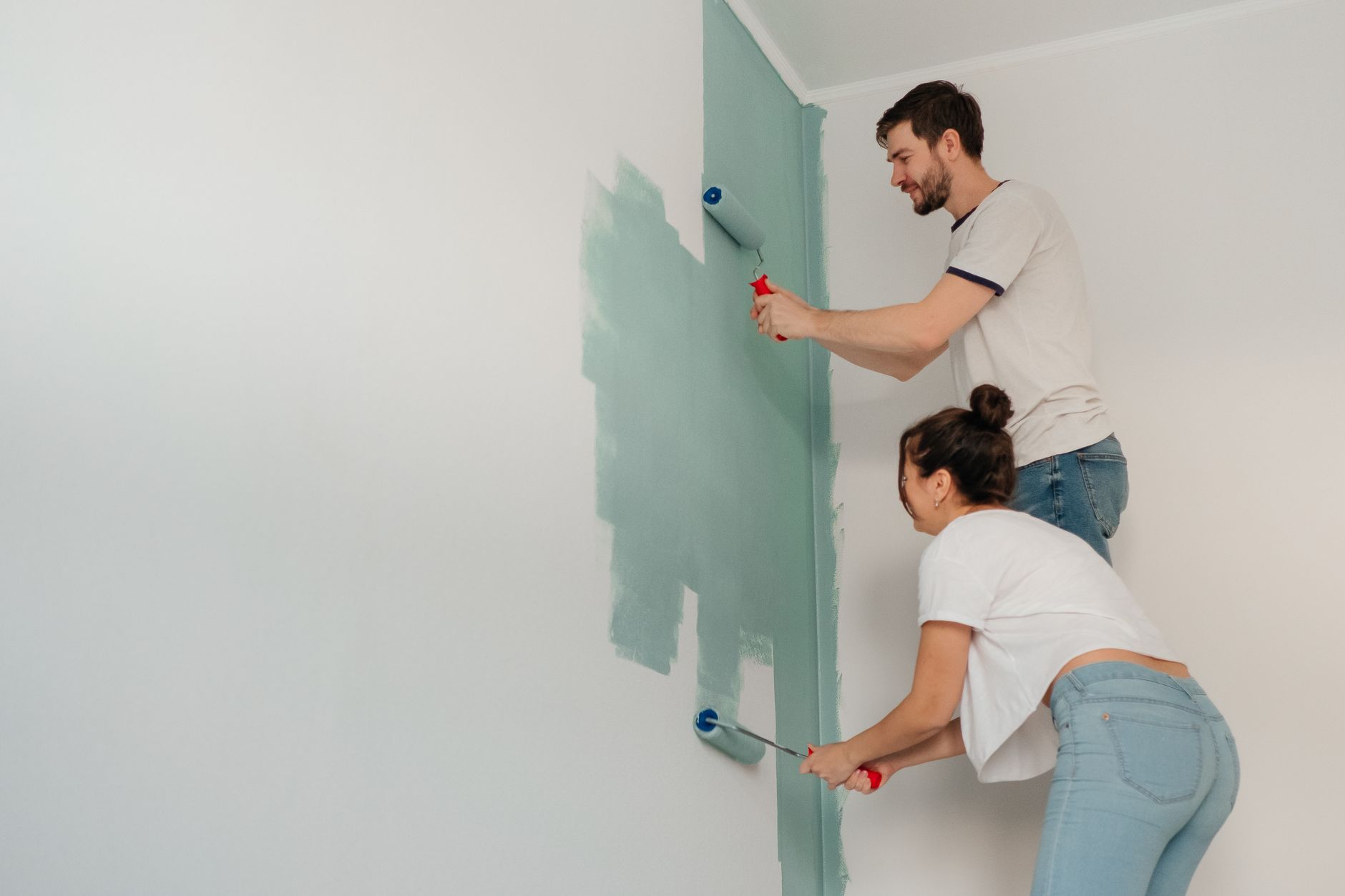 A young couple collaborates on painting a wall with rollers, highlighting teamwork and home improvement. — Vavada promokoodid