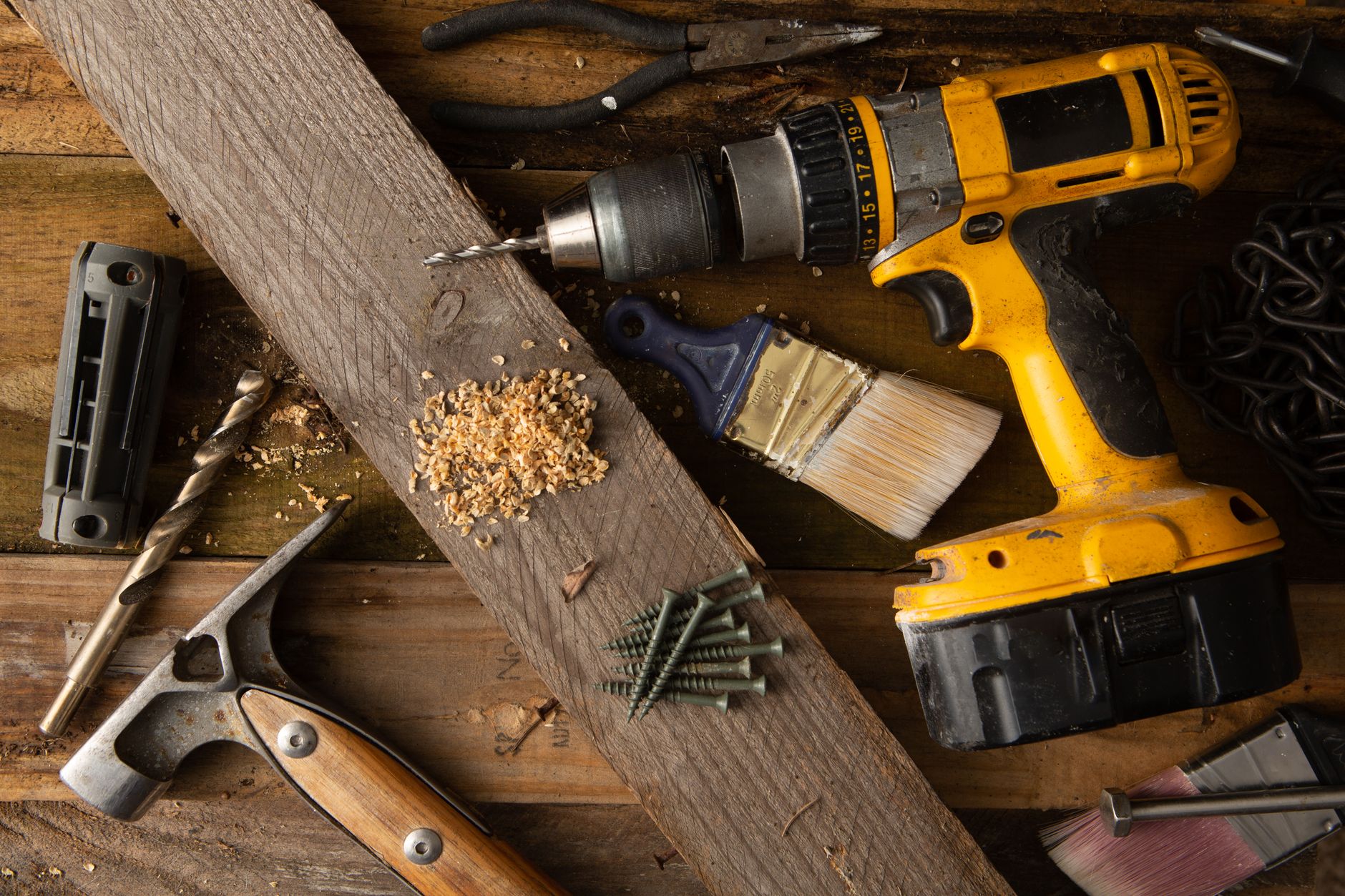 A close-up of various tools including a drill, hammer, and paintbrush on a wooden workbench. — Waterproofing Your Crawl Space